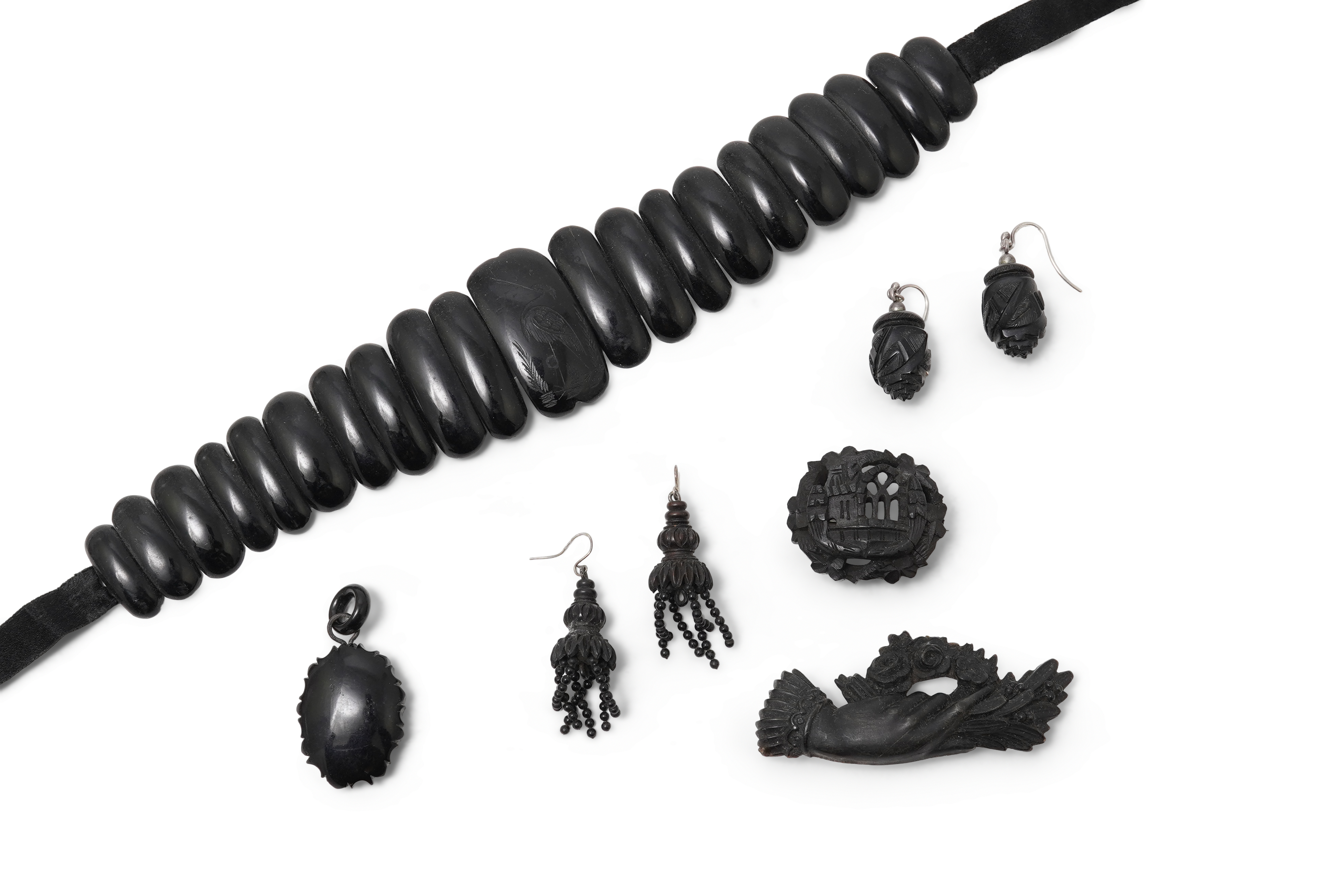 A collection of jewels, comprising: a moulded bog oak brooch depicting a hand holding a posy, length 7.4cm; a carved jet brooch depicting a Gothic ruin, possibly part of Whitby Abbey; a necklace composed of polished pane